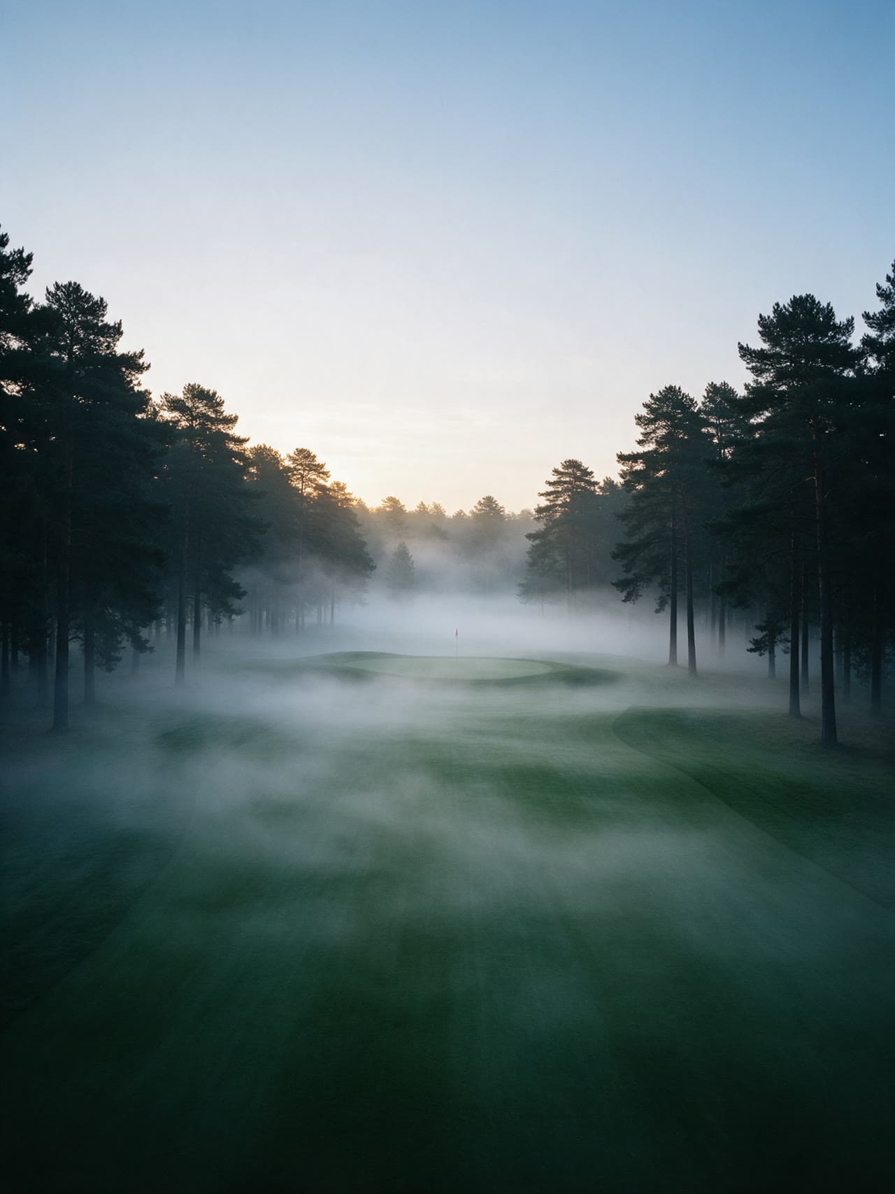 Golf course fairway at sunrise, ground mist drifting over the green